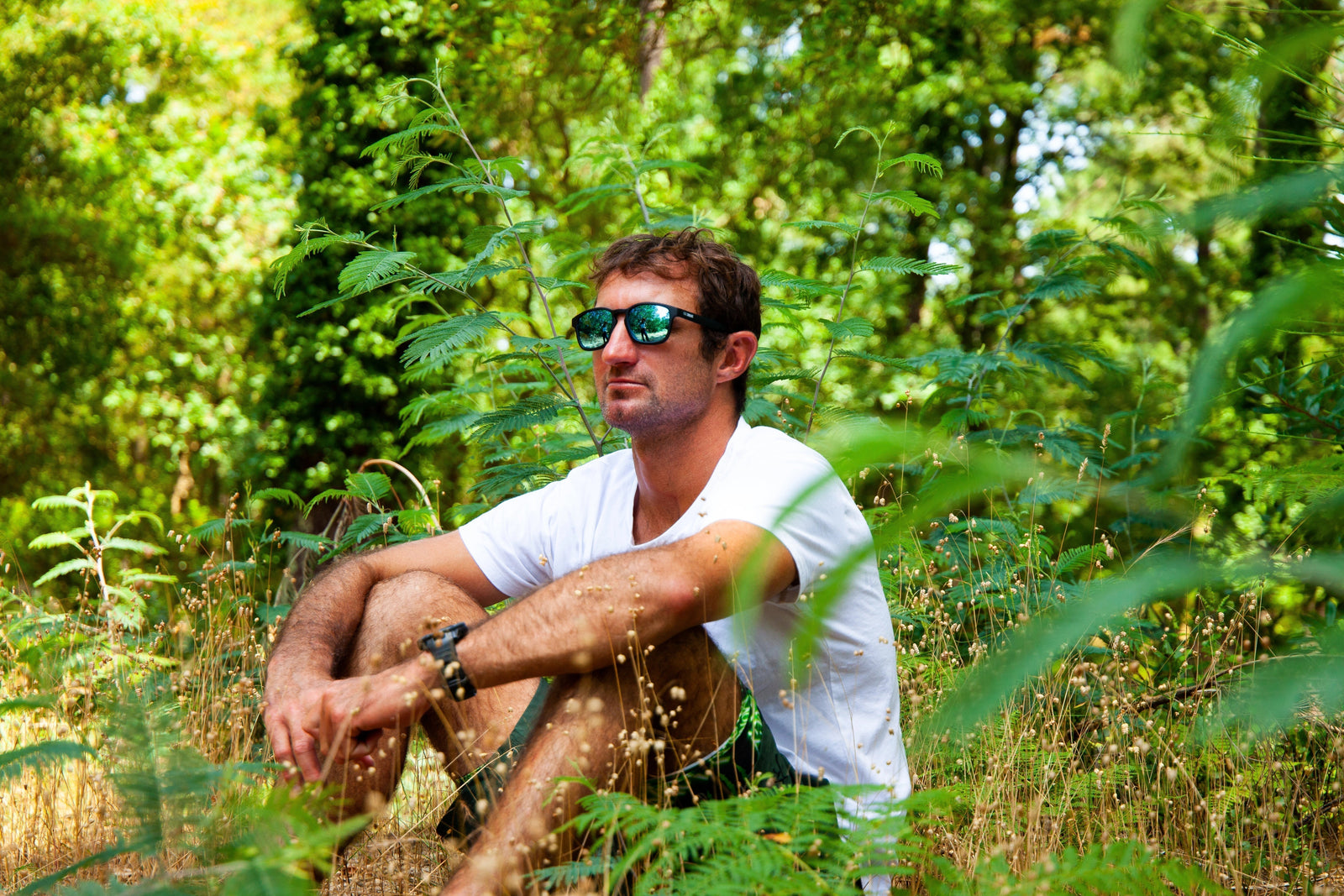 Joan Duru assis dans la forêt landaise portant des lunettes de soleil 2NDLIFE modèle Estran Iceberg